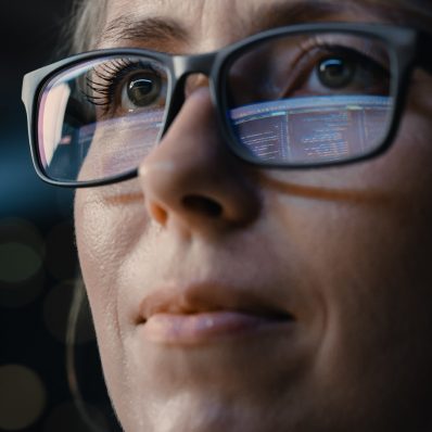 Close-up of a woman's face wearing glasses with screen reflections visible on the lens.