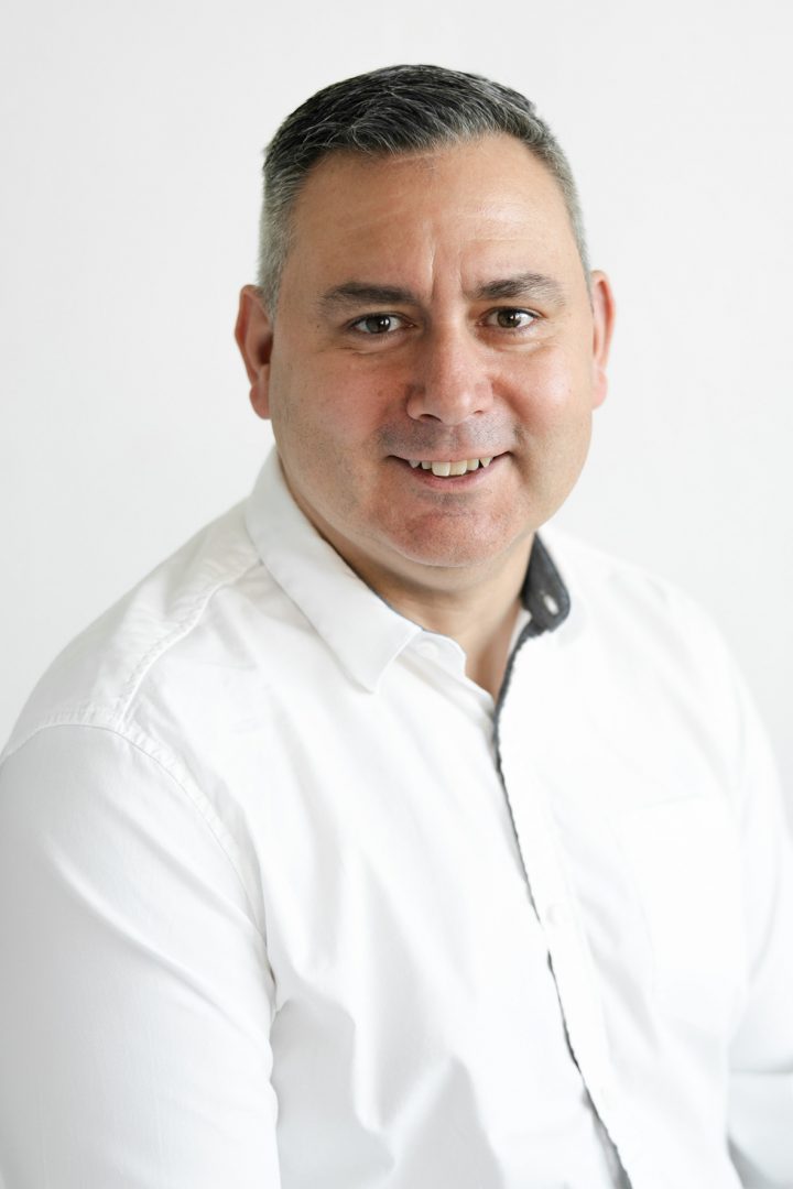 A man in a white shirt smiling at the camera against a white background.